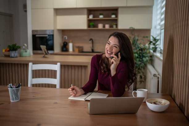 快乐的女人在家中一边打电话一边工作图片 快乐的女人在家中一边打电话一边工作图片下载