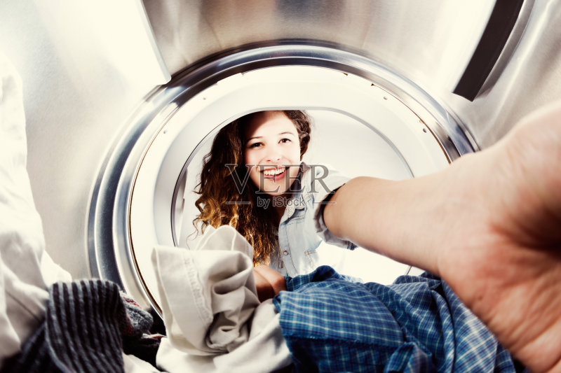 微笑的年轻美女负载衣服烘干机,从里面的鼓正版图片素材