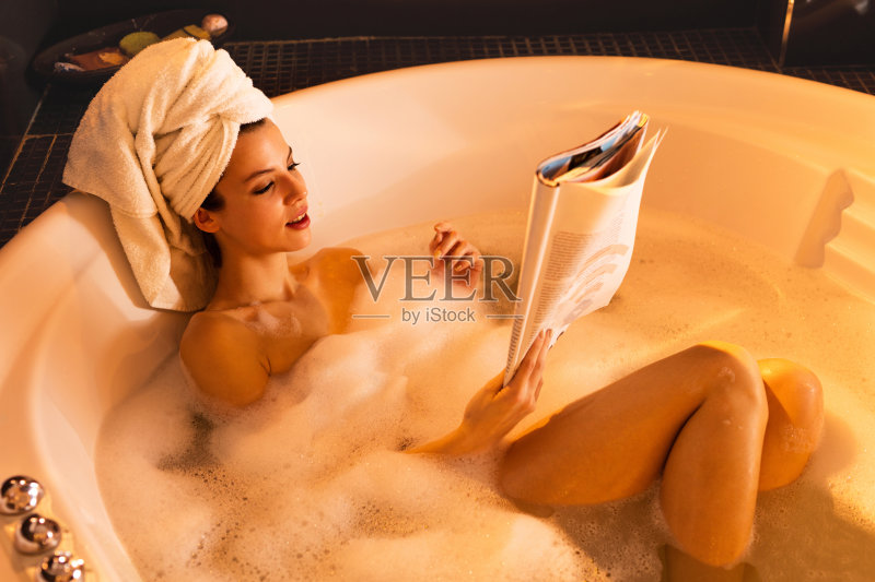 年轻女子在浴缸里放松,看杂志。正版图片素材