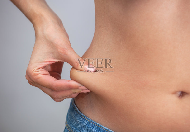 女孩用手拉着腹部的皮肤,露出腹部和两侧的身体脂肪正版图片素材