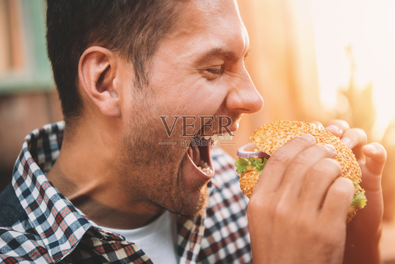 特写侧面的年轻人持有和咬美食自制汉堡包正版图片素材
