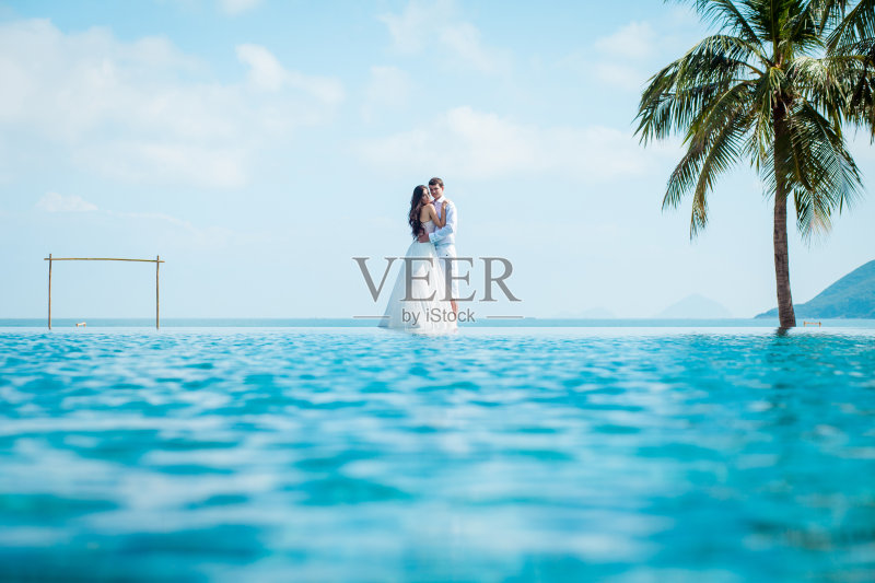 新婚夫妇在豪华度假村举行婚礼后。浪漫的新娘和新郎在游泳池附近放松。蜜月。正版图片素材