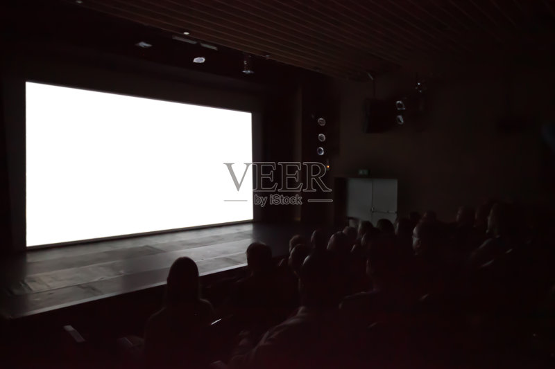 背景模糊的人看电影在电影院的白色屏幕。正版图片素材