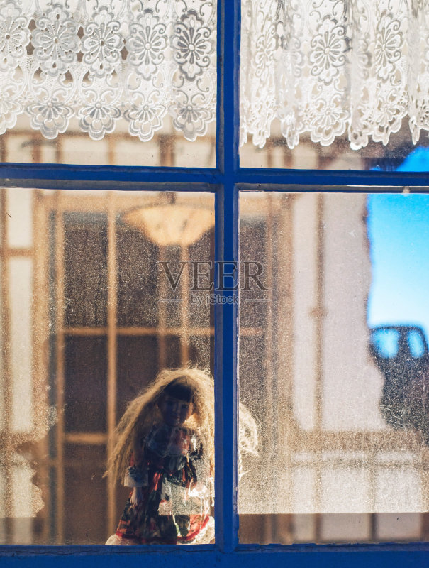 诡异的古董娃娃在老空房子的窗户后面。正版图片素材