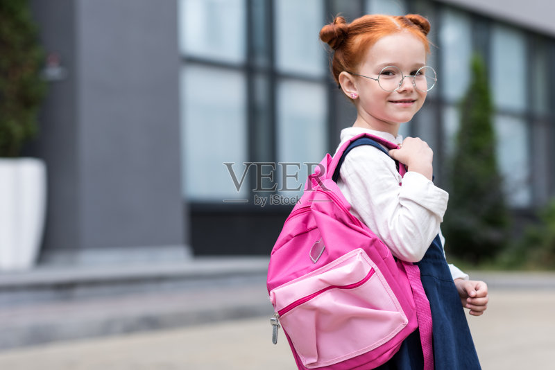 戴眼镜的可爱红发女学生拿着背包对着镜头微笑照片摄影图片