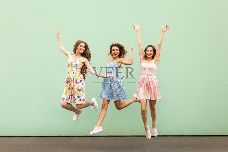 时尚年轻女性的跳跃和举起手。看着镜头,露出露齿的微笑正版图片素材