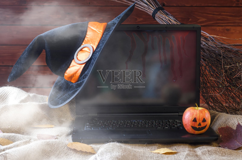 万圣节的概念:一台笔记本电脑,一顶女巫帽和一把扫帚,为你的广告提供免费空间。正版图片素材