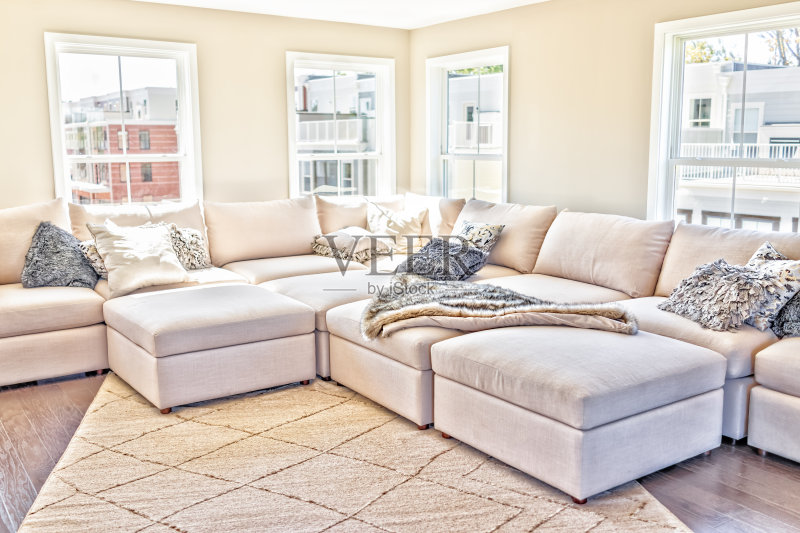 现代公寓、住宅或家庭的阁楼室内空间,摆放着米色、中性白色的大沙发和带枕头的地毯正版图片素材