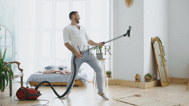 一个年轻人和吸尘器一起打扫屋子,跳舞的样子像个吉他手正版图片素材