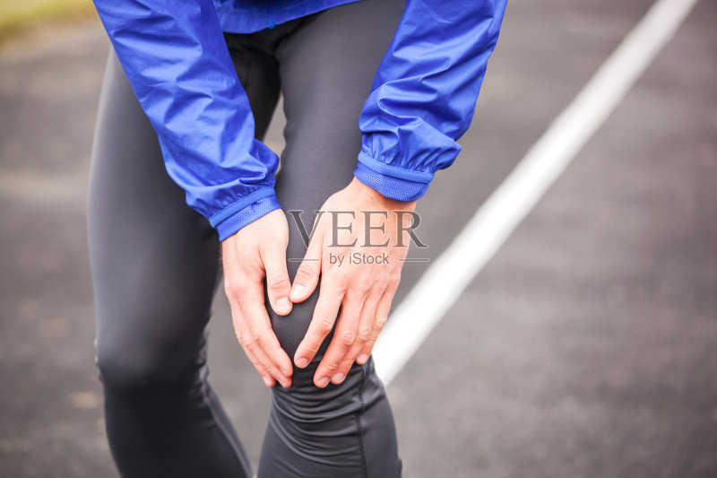 一个年轻的跑步者在跑步时抱着他受伤的膝盖。正版图片素材