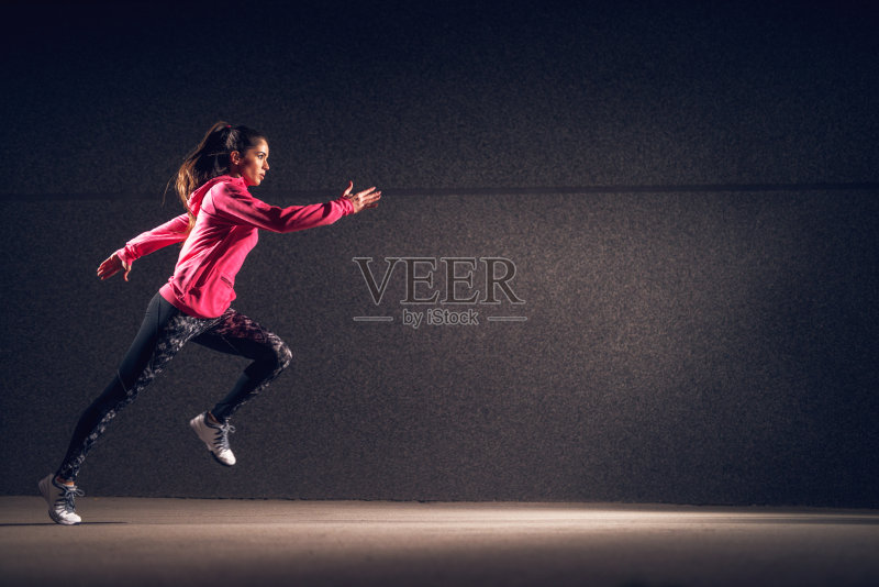 侧运动的年轻性感迷人的健康的健身运动积极的苗条的女孩与运动服跑在灰色的墙在晚上的街道。正版图片素材