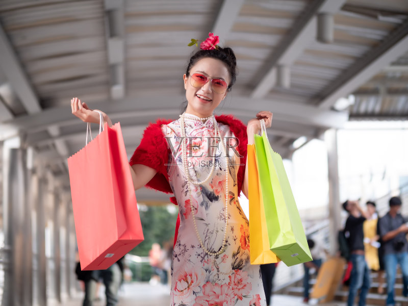 在泰国曼谷市中心,年轻的亚洲女子穿着中式服装,拿着购物袋。中国新年与购物概念正版图片素材