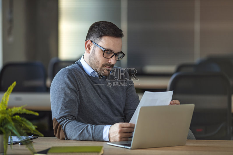 一个年轻人坐在办公室的办公桌前。正版图片素材