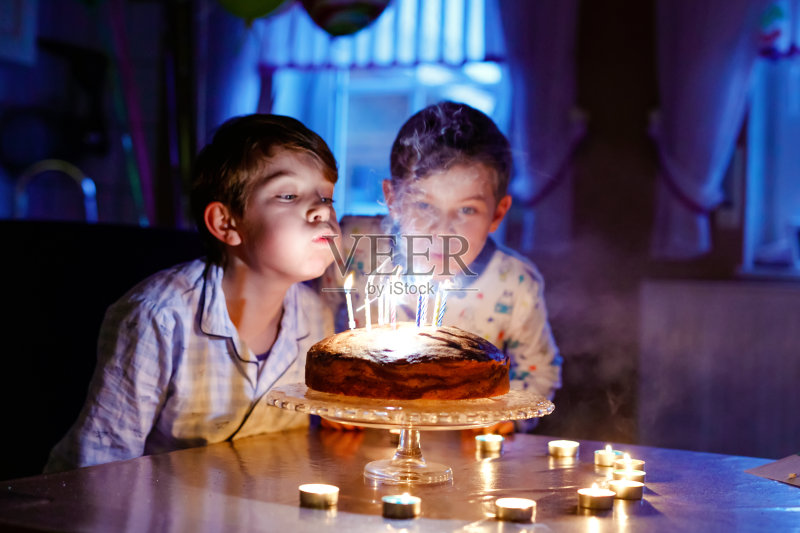 两个快乐的金发小男孩庆祝生日。在室内,孩子们在自制的烤蛋糕上吹蜡烛。孩子们的生日派对,双胞胎的家庭庆祝正版图片素材