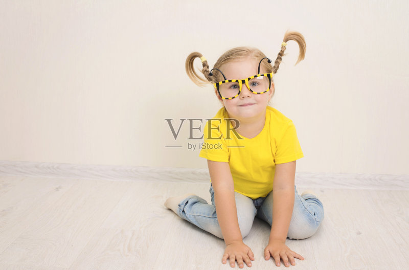 快乐有趣的小女孩,戴着派对蜂眼眼镜,梳着有趣的辫子,穿着黄色t恤和牛仔裤。正版图片素材