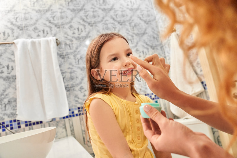 年轻母亲在女儿的皮肤上涂抹面霜正版图片素材