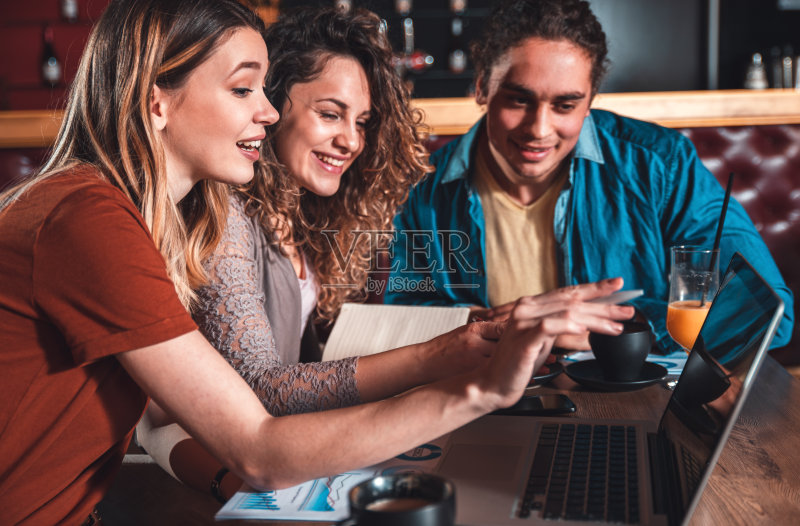 一群学生坐在咖啡馆里用笔记本电脑喝着咖啡,谈论着下一个项目。正版图片素材