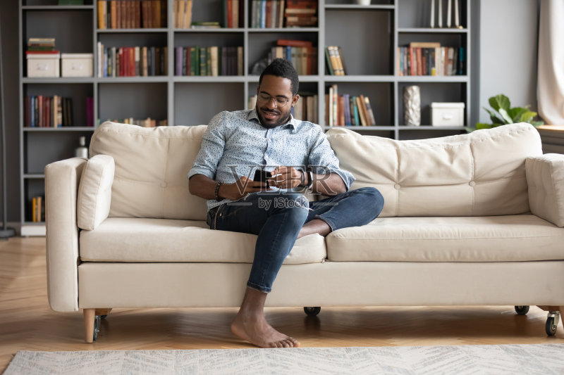 微笑的非洲年轻人坐在舒适的沙发上,玩游戏。正版图片素材