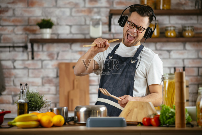 英俊的年轻人一边做饭一边听音乐。正版图片素材