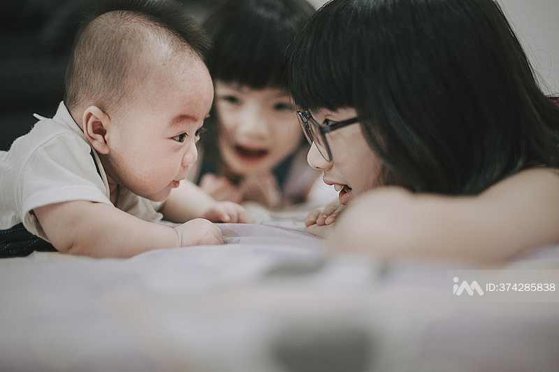 三个华人家庭的兄弟姐妹在床上玩耍照片摄影图片