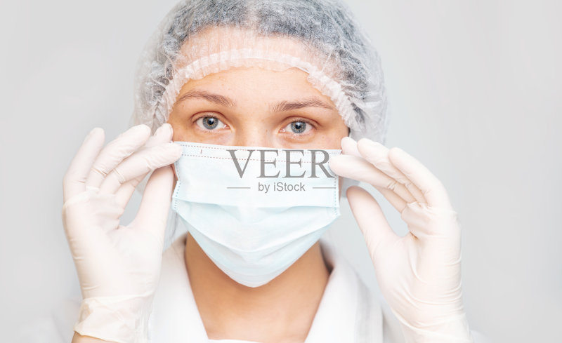 一个成年妇女的肖像在一个孤立的背景上戴着医用口罩、手套和帽子正版图片素材