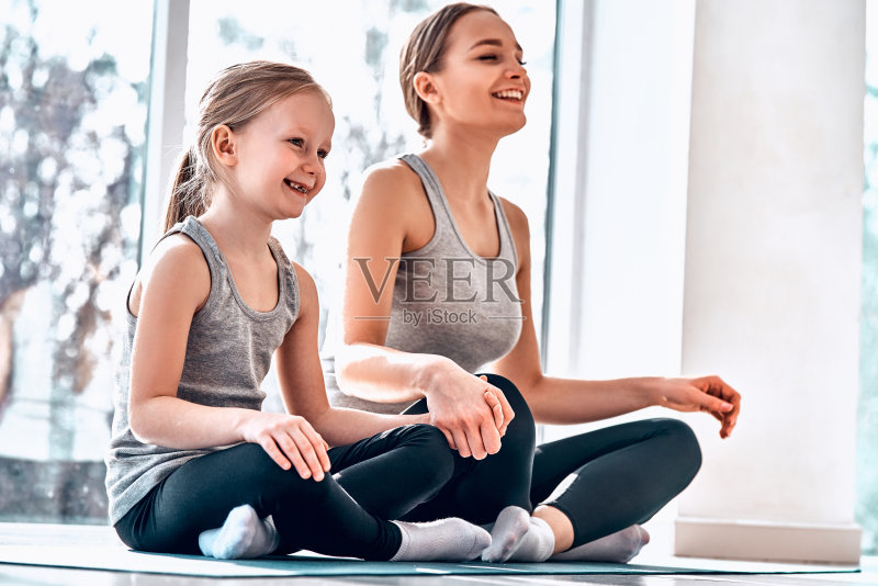 年轻的母亲和她3岁的女儿坐在窗前的窗台上,摆着莲花姿势正版图片素材