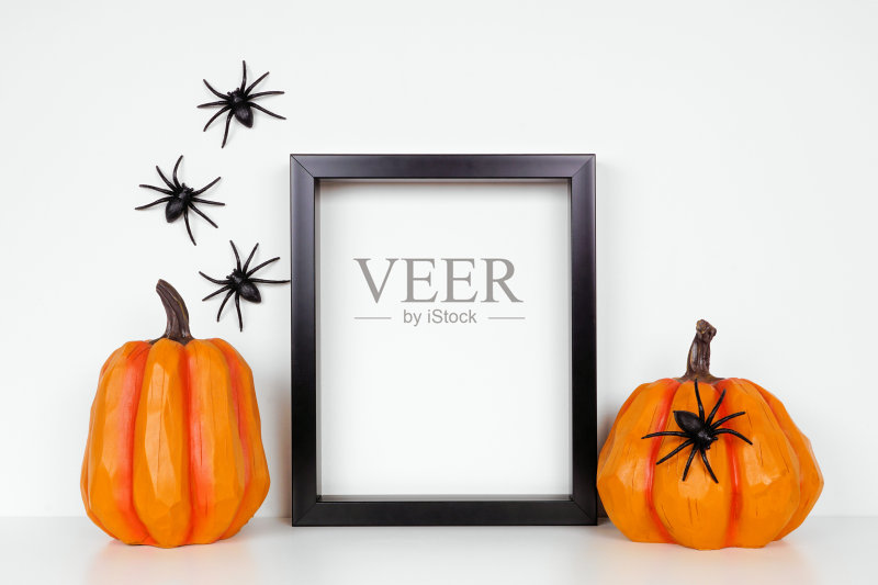用万圣节南瓜装饰的黑色框架在架子上或桌子上,靠着一堵有蜘蛛的白墙正版图片素材