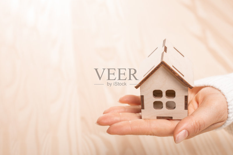 女人手握小木制玩具屋,在天然木制模糊的背景上正版图片素材