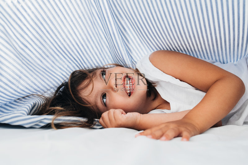 快乐的年轻女孩在被单上醒来正版图片素材