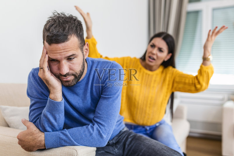 年轻夫妇争吵——冲突、不良关系。愤怒的女子。年轻夫妇坐在客厅的沙发上,因误解而争吵照片摄影图片