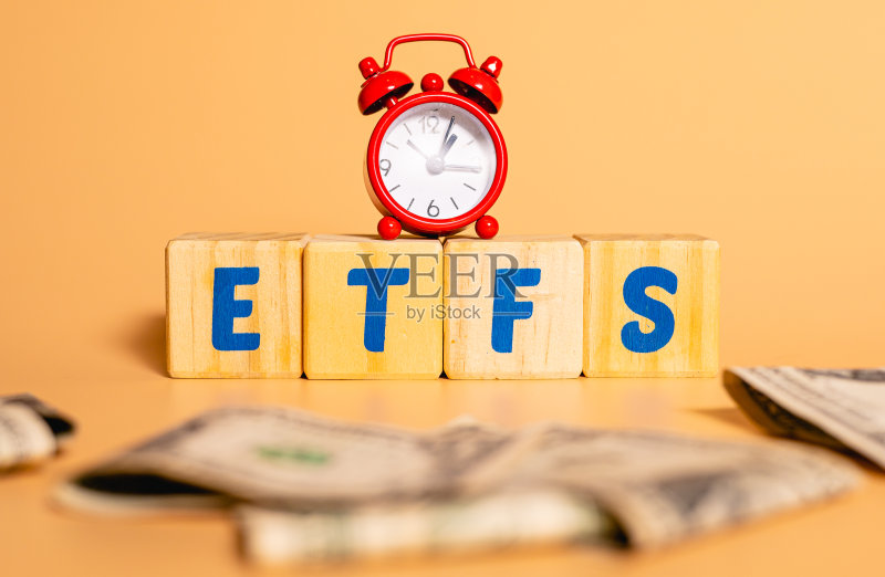 木制方块上的英文文字:ETFS(交易所交易基金),闹钟和美元,经济与投资概念照片摄影图片