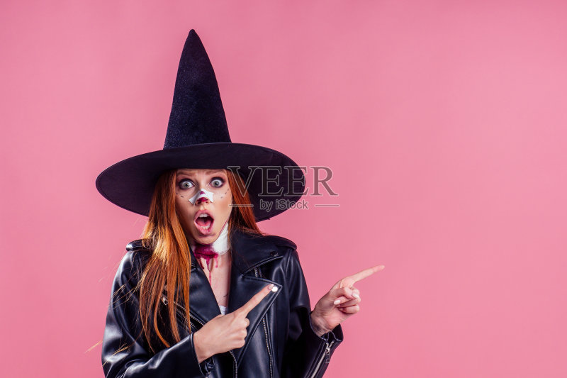 惊讶和惊讶的红头发姜女人女巫黑色帽子和皮夹克尖叫和恐惧与疯狂的化妆在她的漂亮的脸在工作室粉红色的背景副本spase正版图片素材