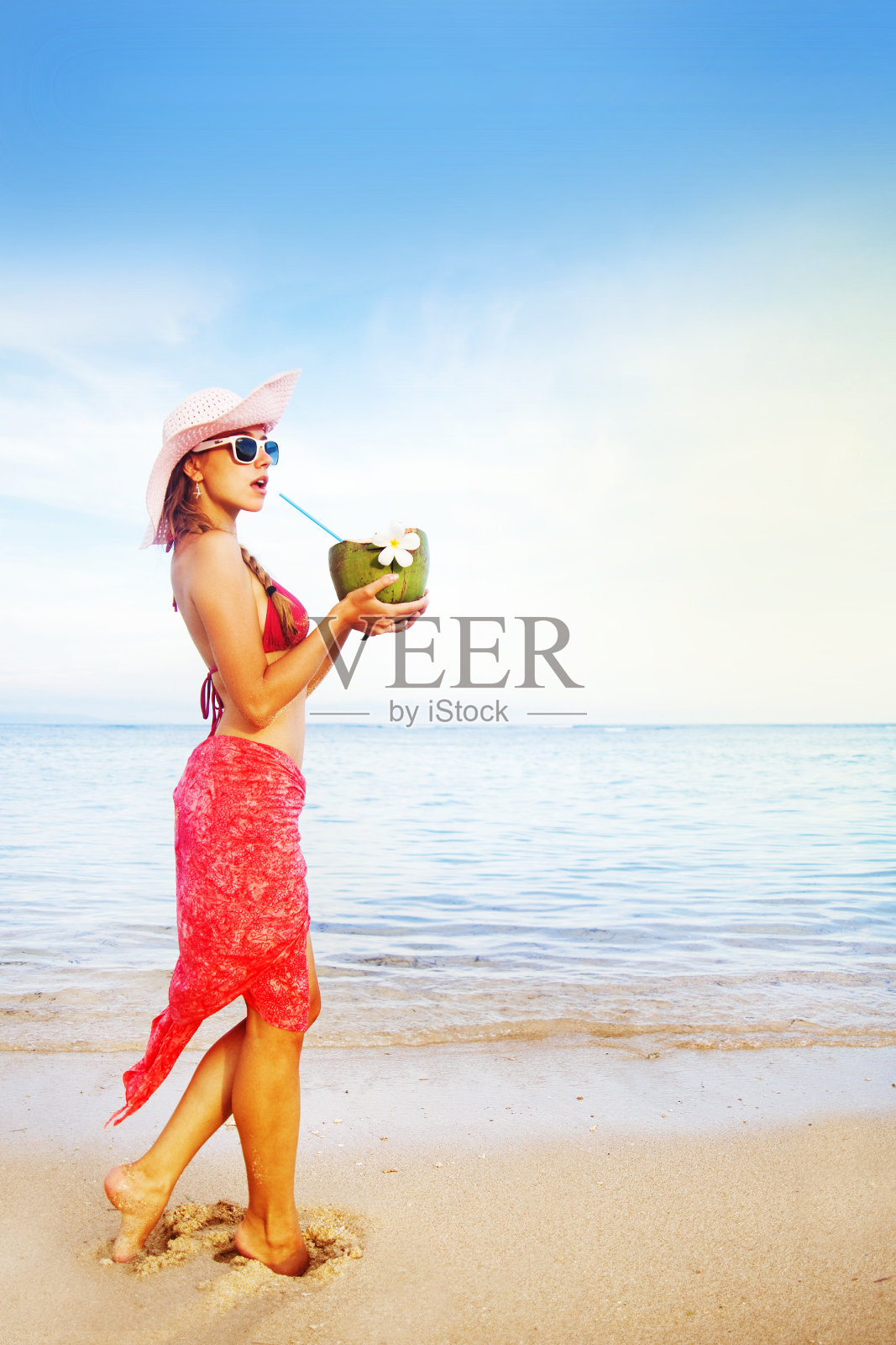 年轻女子穿着粉红色泳衣，喝着椰子鸡尾酒照片摄影图片