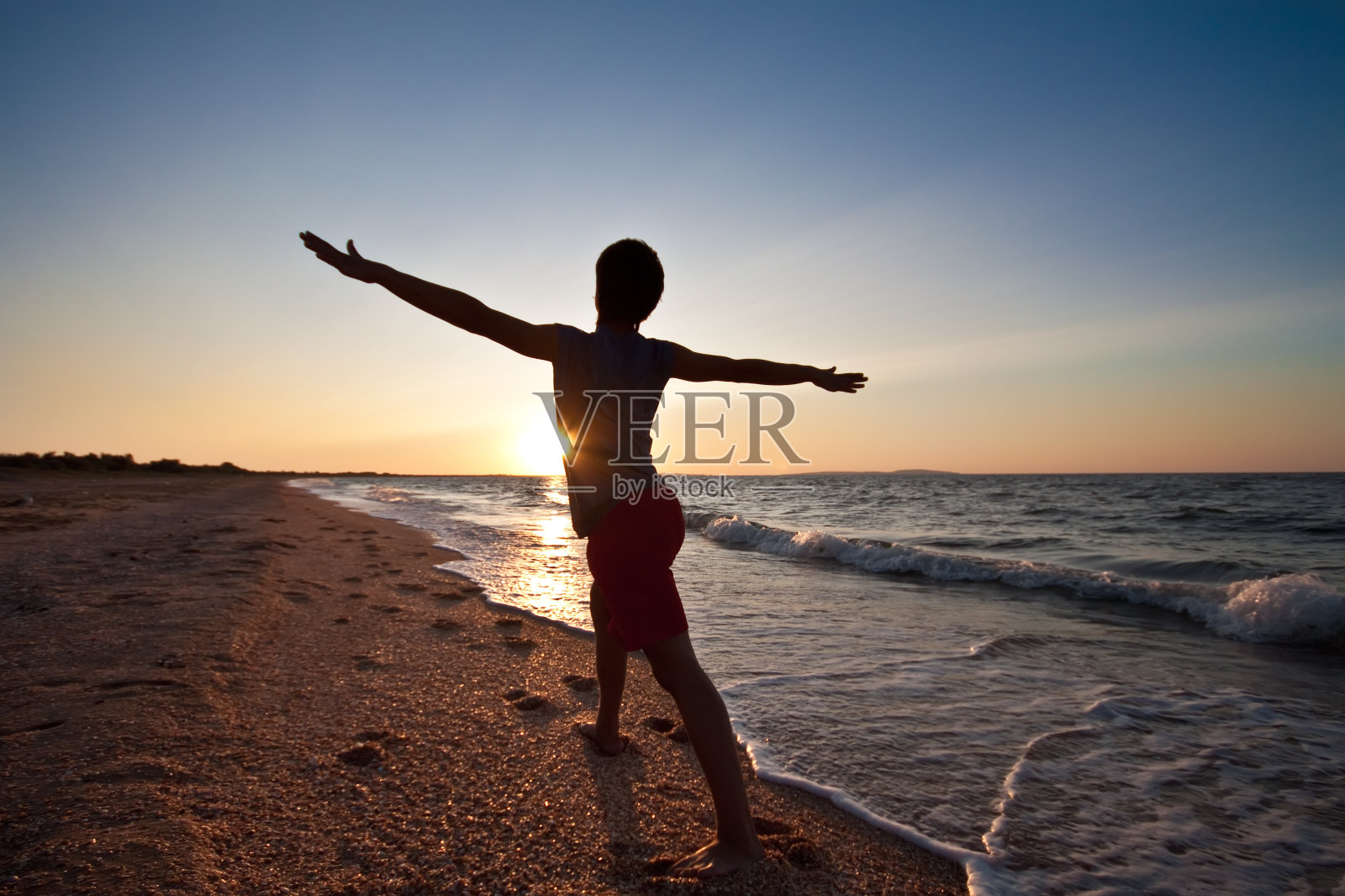 一个少年在海滩上对着日落沉思照片摄影图片