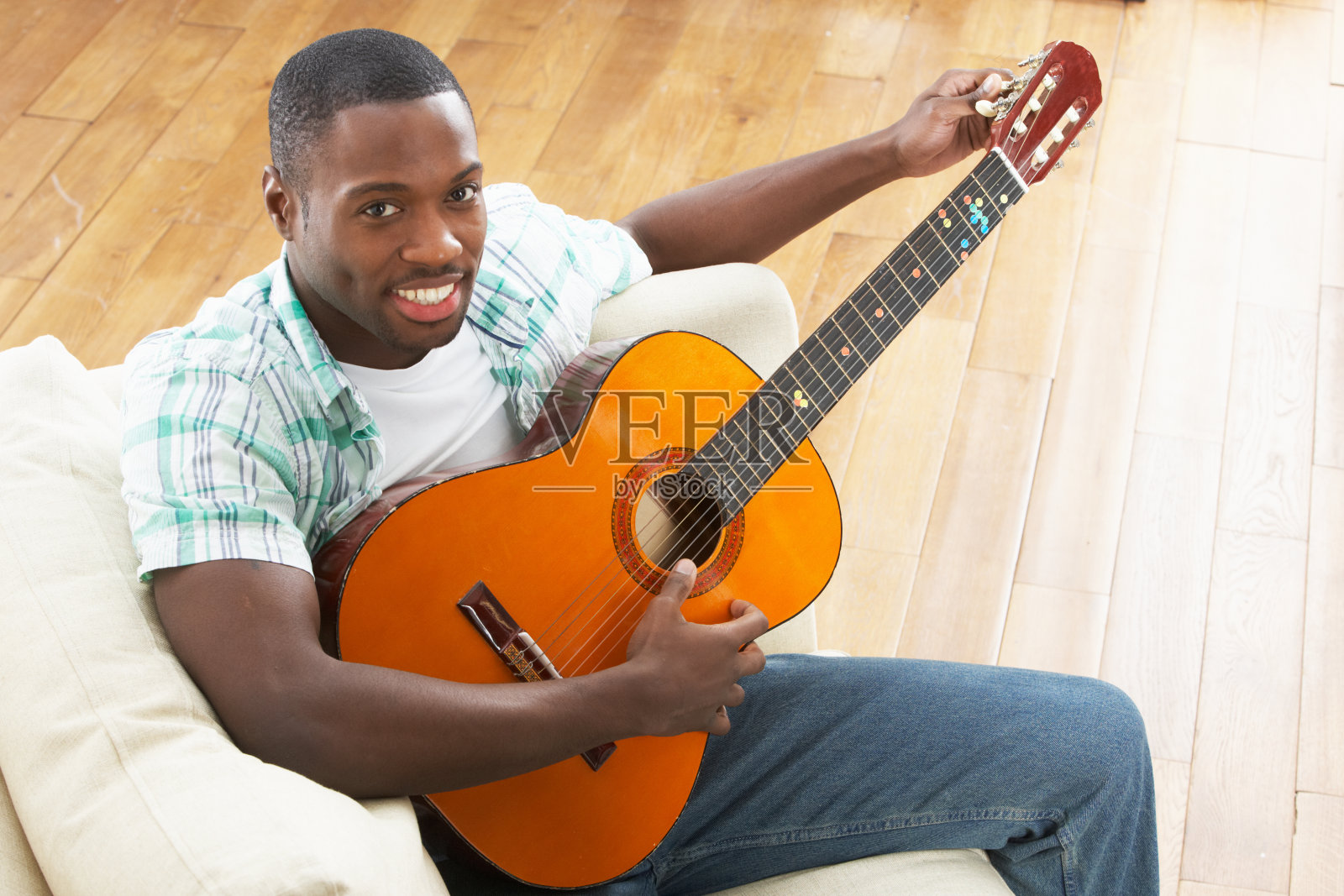 年轻男子坐在沙发上玩原声吉他照片摄影图片