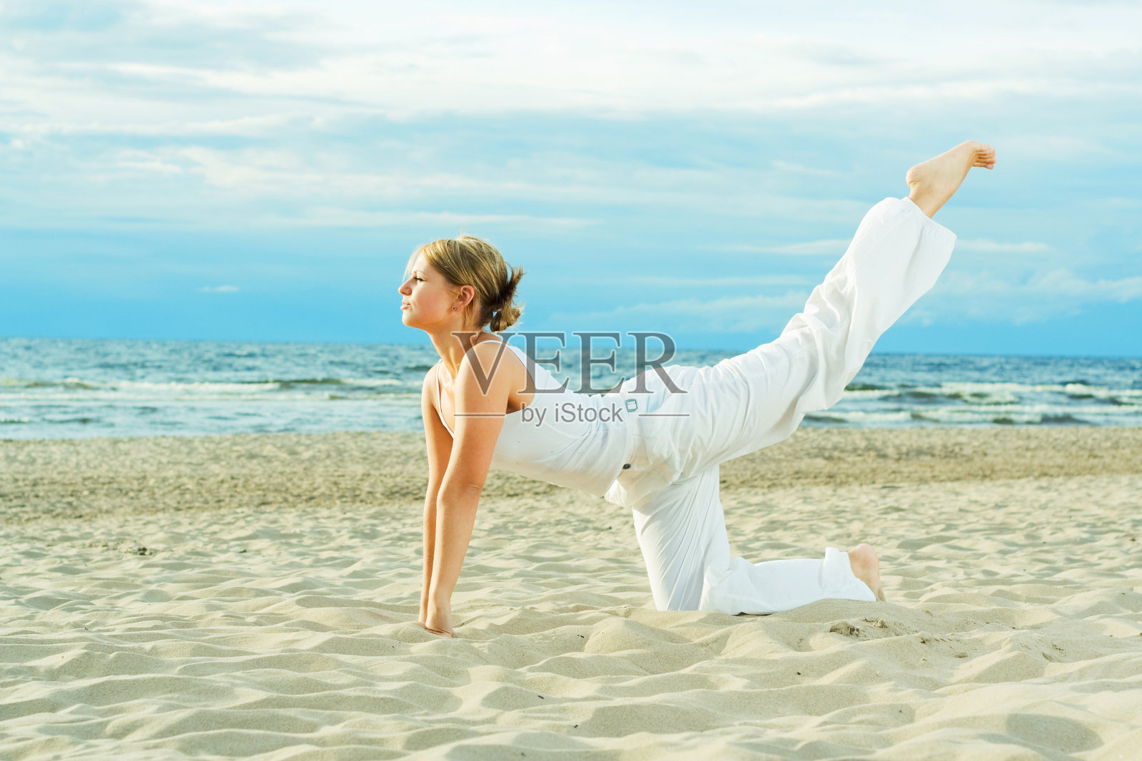 年轻可爱的女孩在沙滩上训练。照片摄影图片