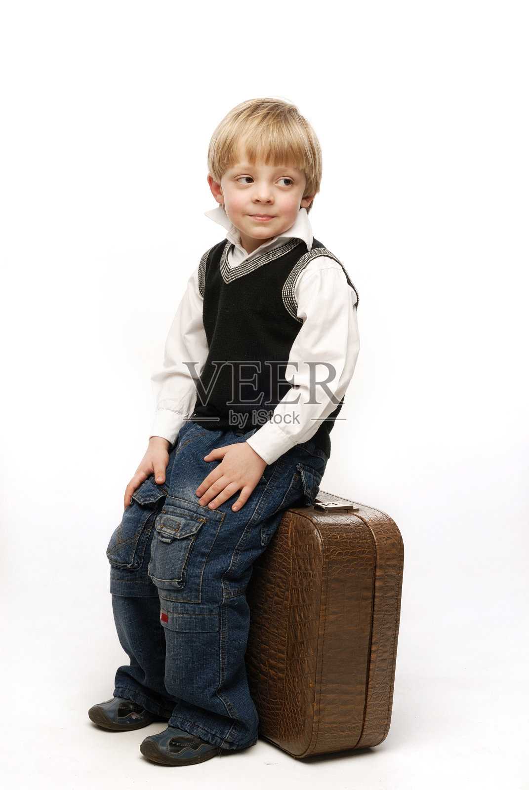 盛装打扮的小男孩竖着坐在皮箱上照片摄影图片