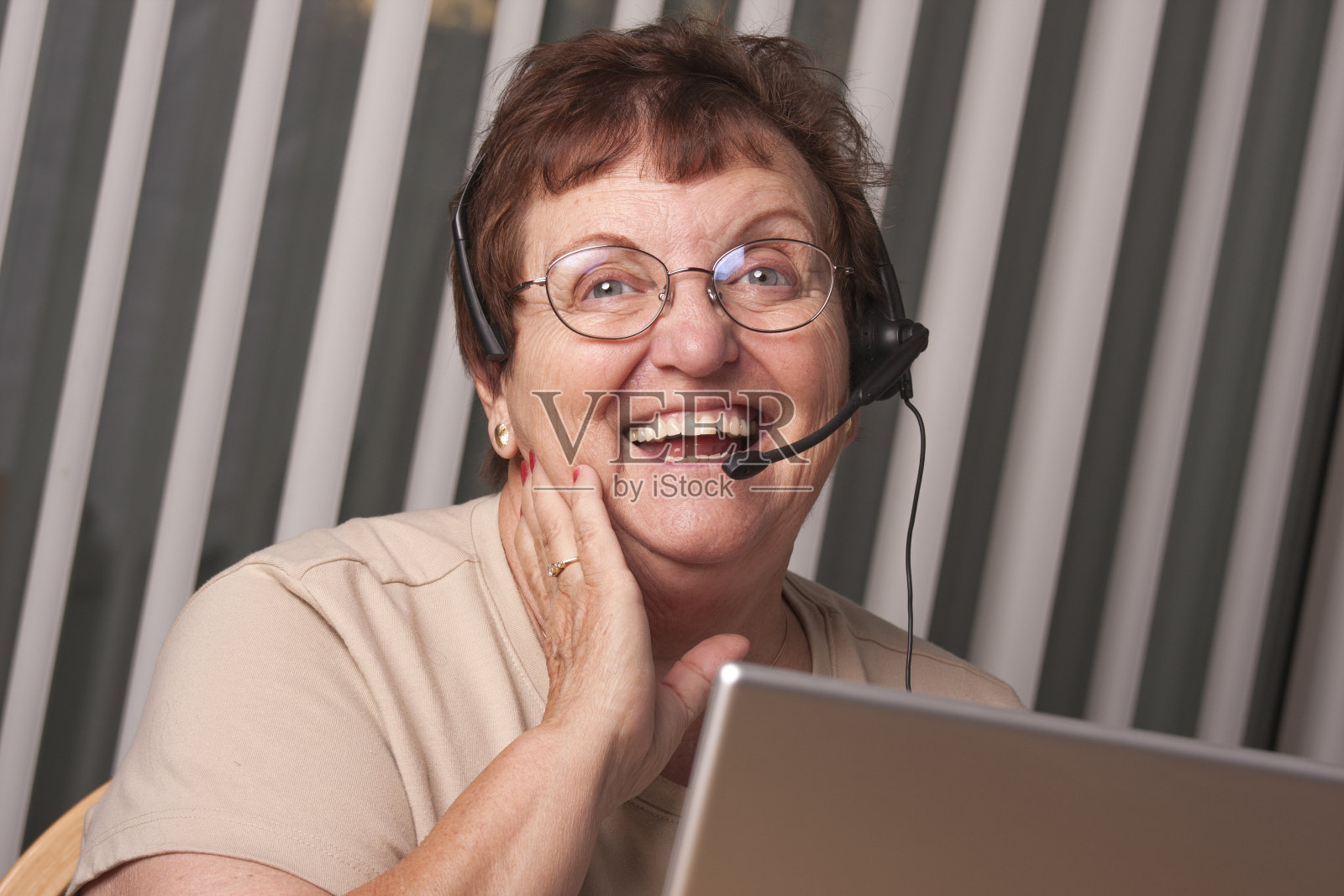 微笑的年长成年妇女与电话耳机和显示器照片摄影图片