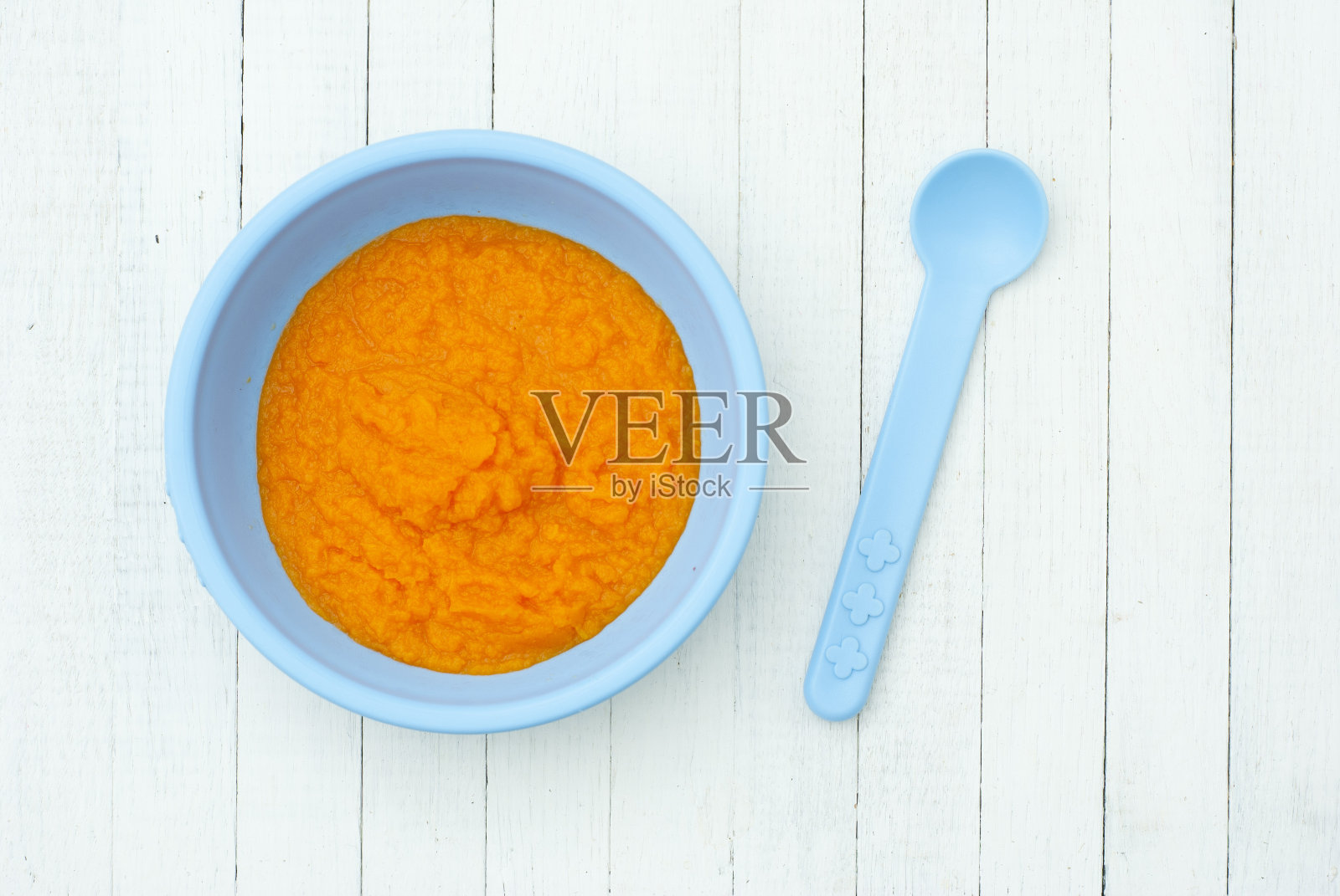 蓝色的碗里装着橙色的婴儿食品，旁边放着蓝色的勺子照片摄影图片