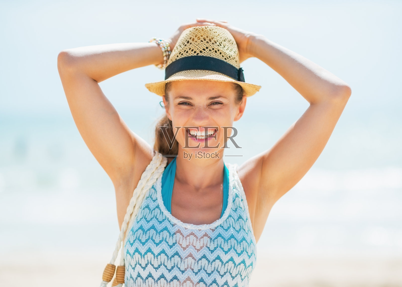 在海滩上戴着帽子微笑的年轻女子的肖像照片摄影图片