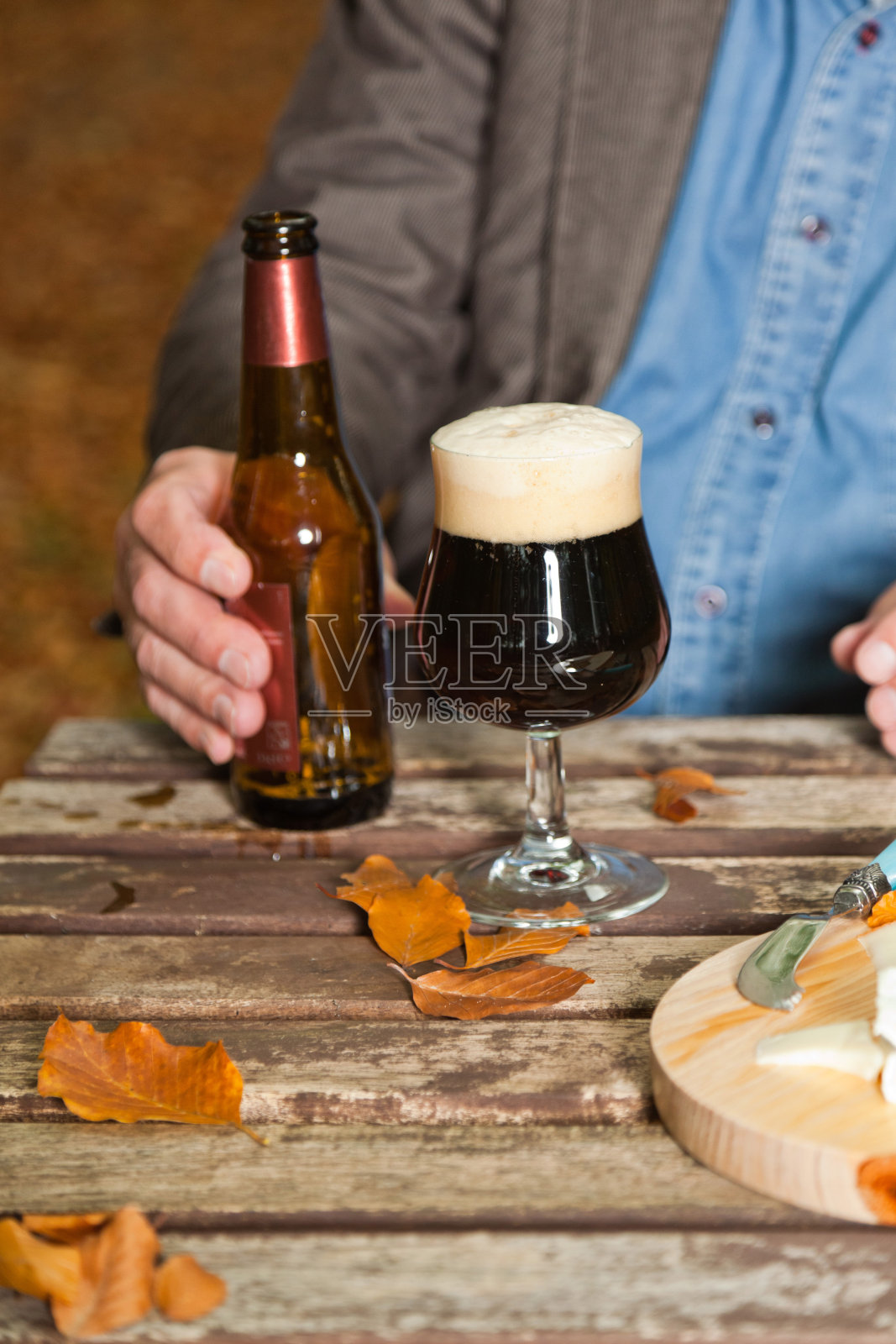 老人在秋天的森林里享用黑啤和奶酪。照片摄影图片