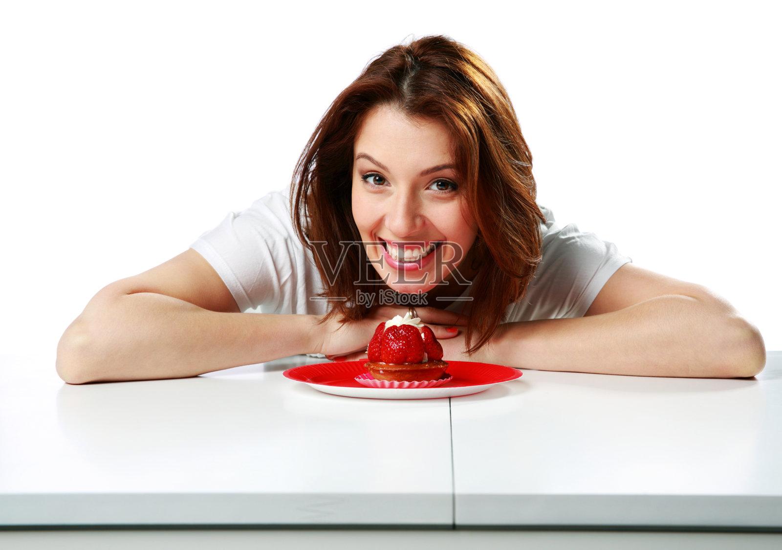 快乐的女人坐在桌上，手里拿着新鲜的草莓蛋糕照片摄影图片