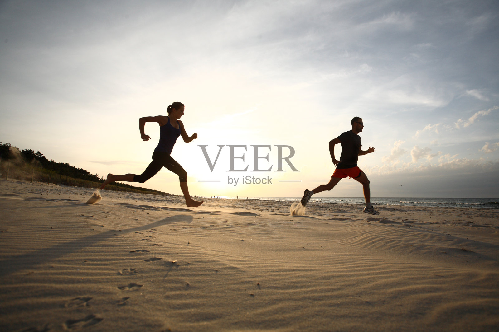日落时分，男人和女人在海滩上跑步照片摄影图片