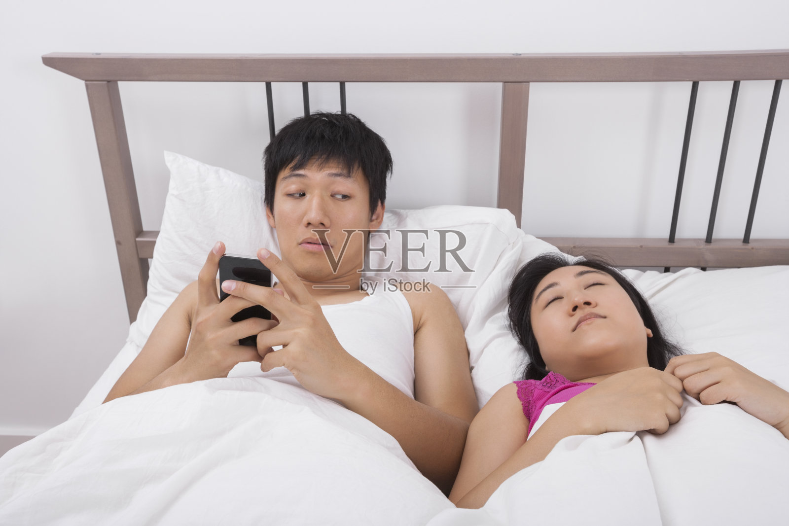 男人一边用手机一边看床上的女人照片摄影图片