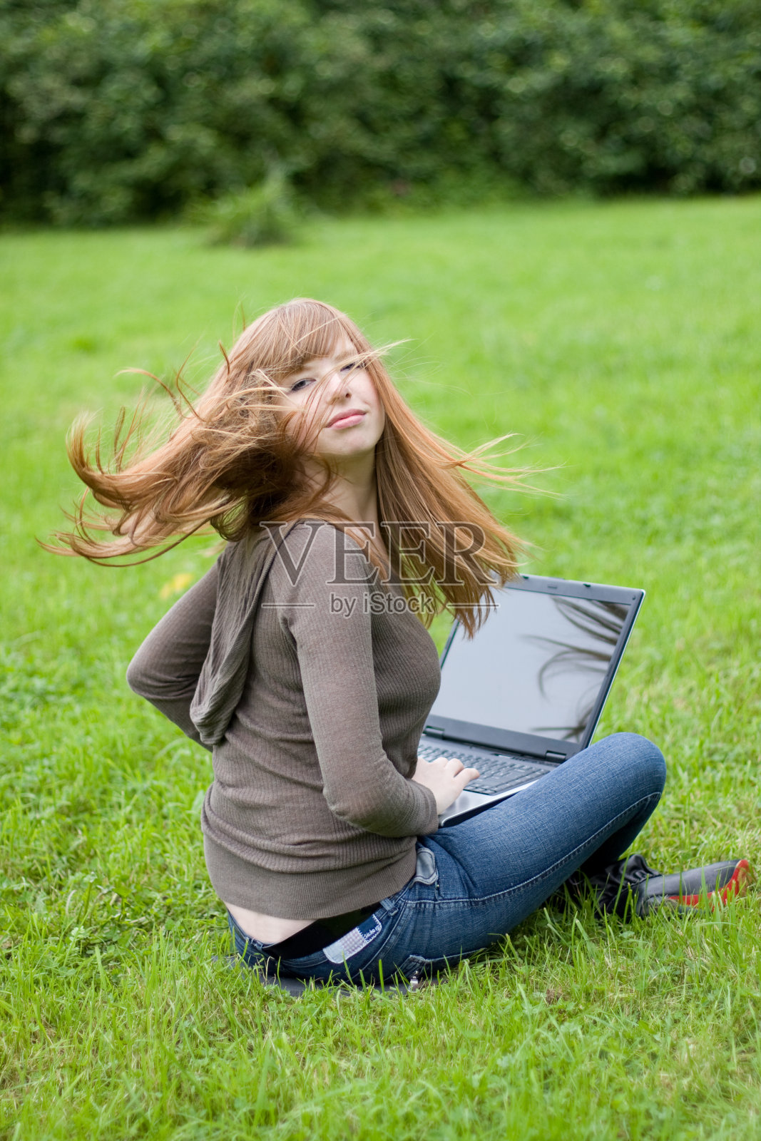 年轻的女孩坐在草地上。照片摄影图片