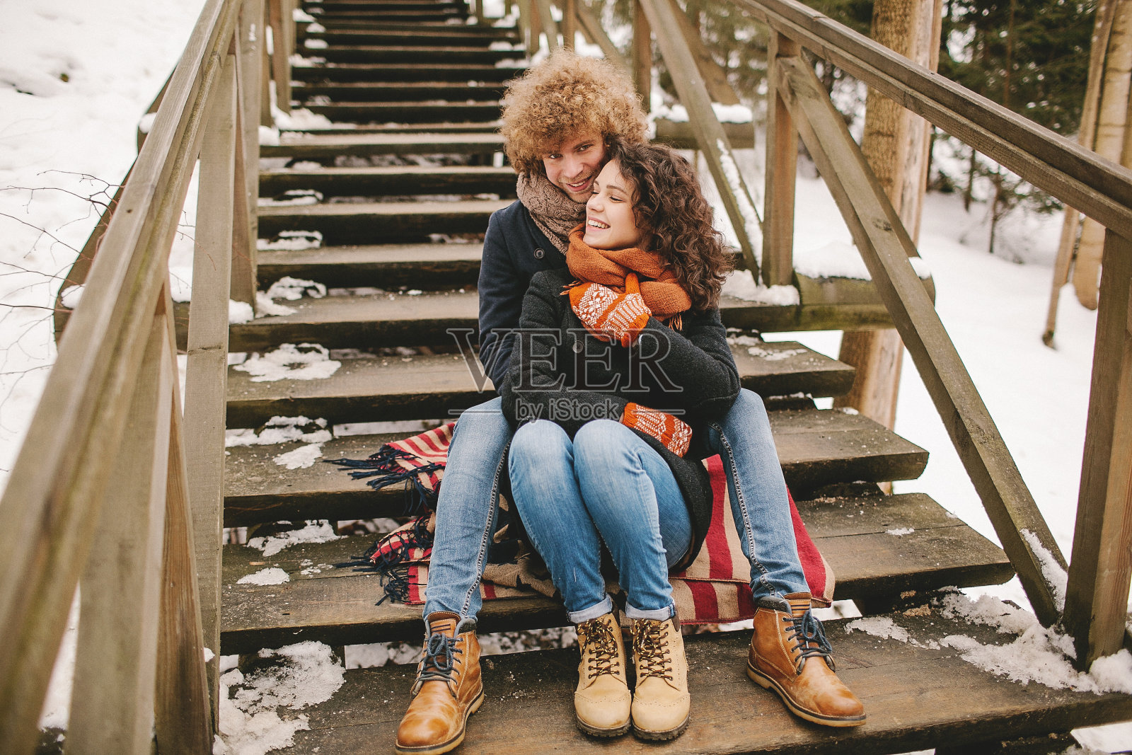 冬天，一对年轻夫妇坐在户外的木楼梯上照片摄影图片