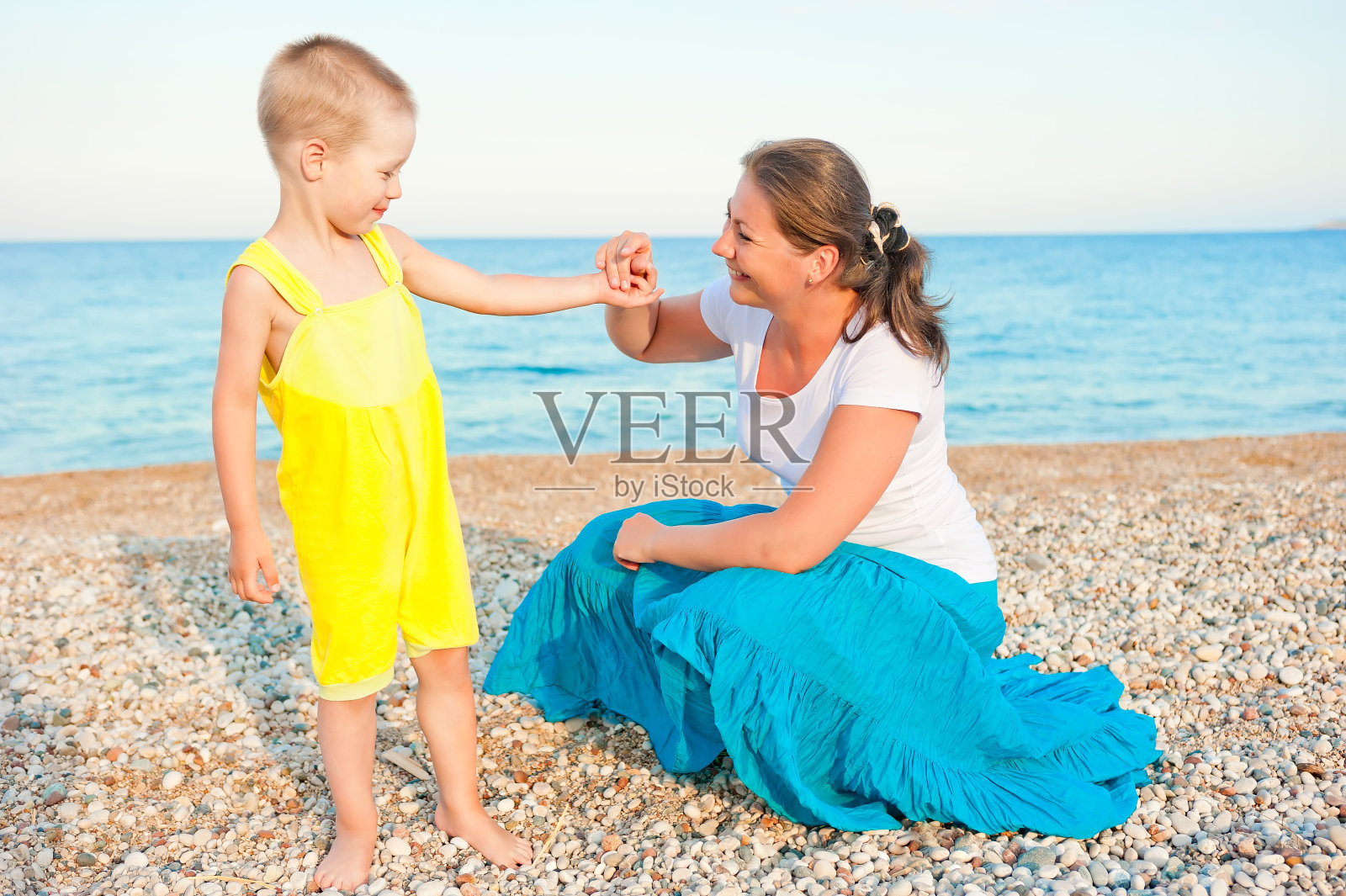 傍晚，母亲和儿子在卵石滩上照片摄影图片