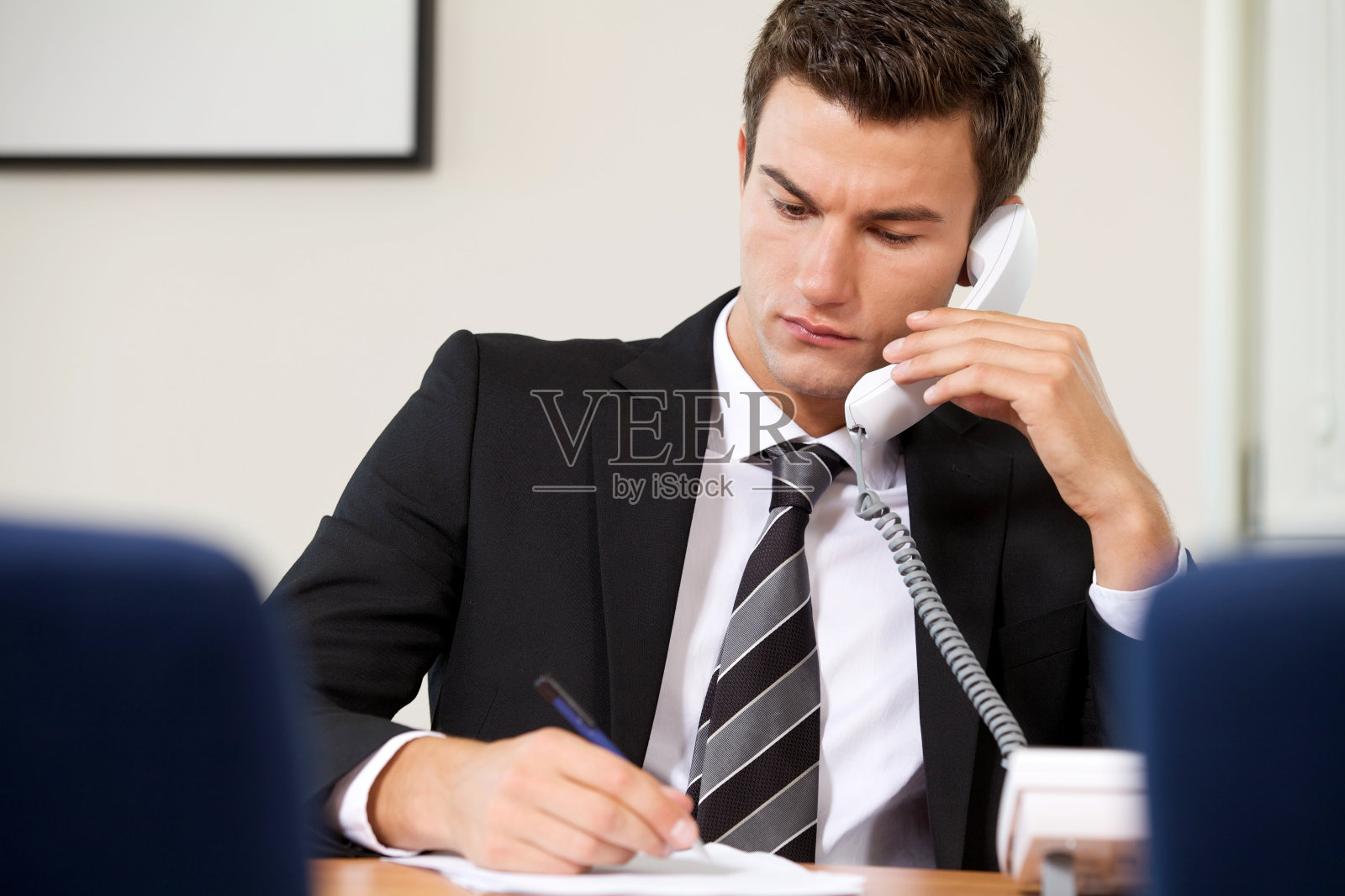 一个年轻的商人一边写东西，一边用电话线打电话照片摄影图片