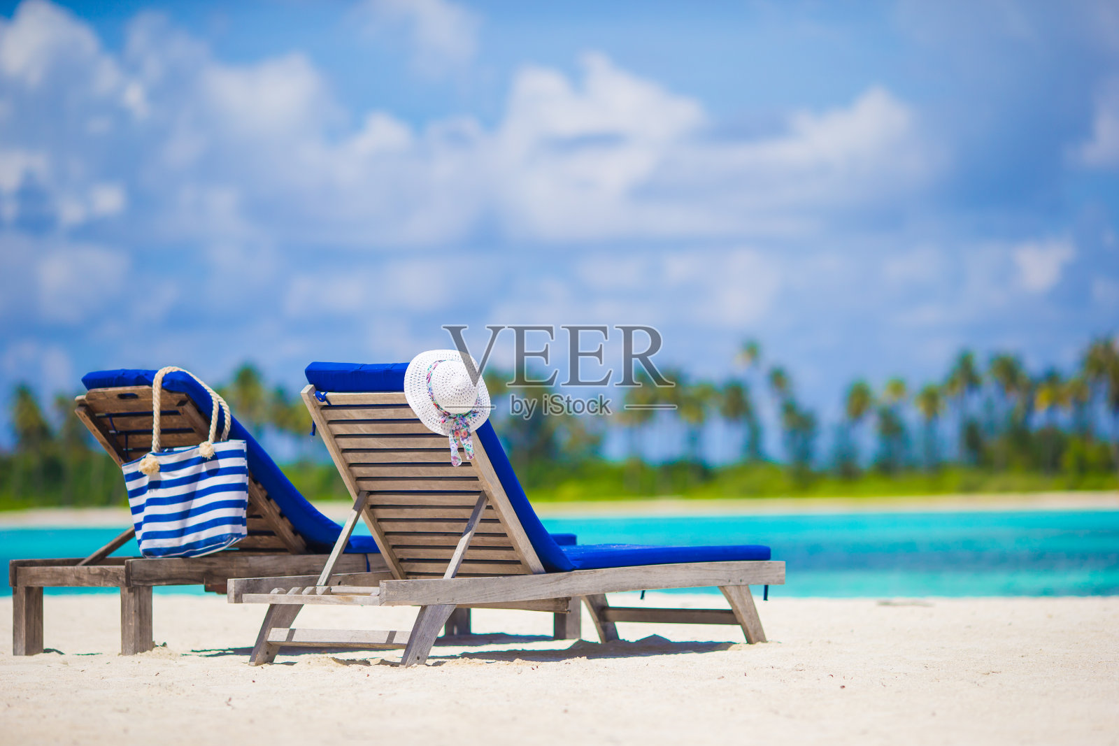 白色沙滩上的木制躺椅、草帽和包照片摄影图片