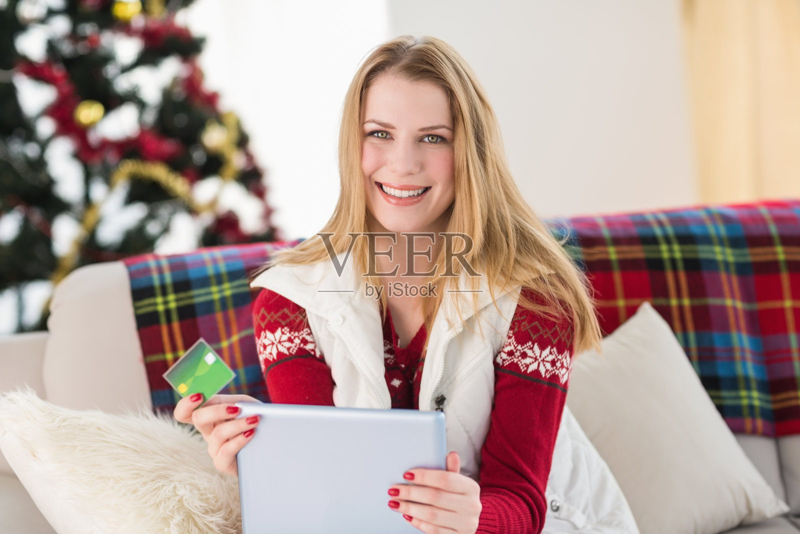 可爱的金发美女坐在沙发上拿着信用卡和平板电脑照片摄影图片